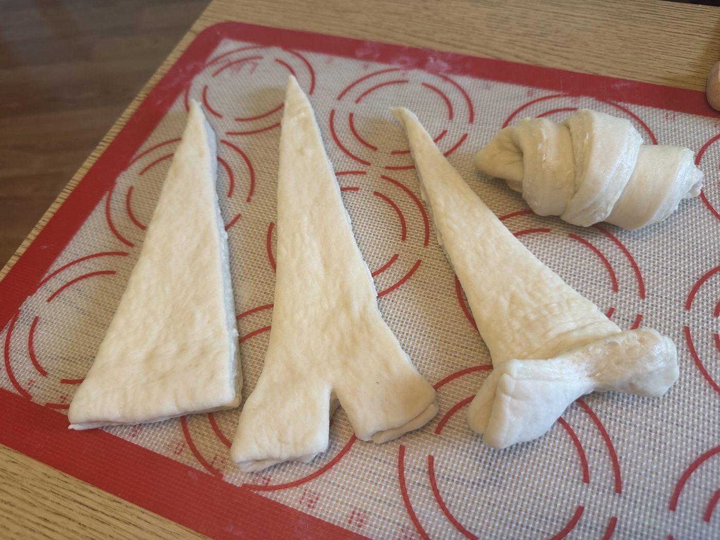 Cheryl Odden's croissant dough cut into triangles with one rolled up, on a silicone baking mat