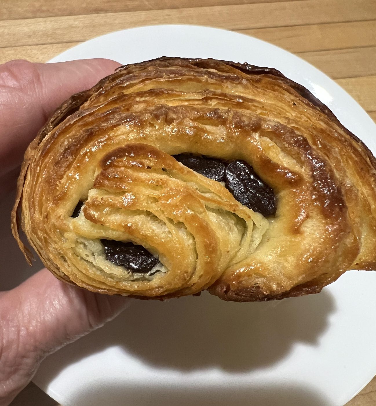 A pain au chocolat torn open, flaky layers and dark chocolate batons inside, held over a white plate