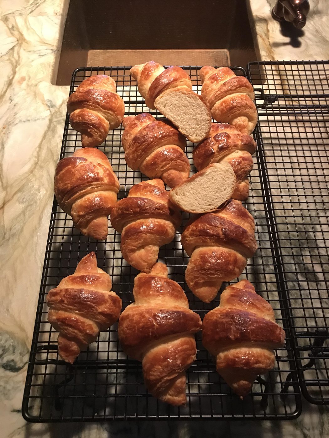 A rack of golden croissants, two sliced open to show the crumb
